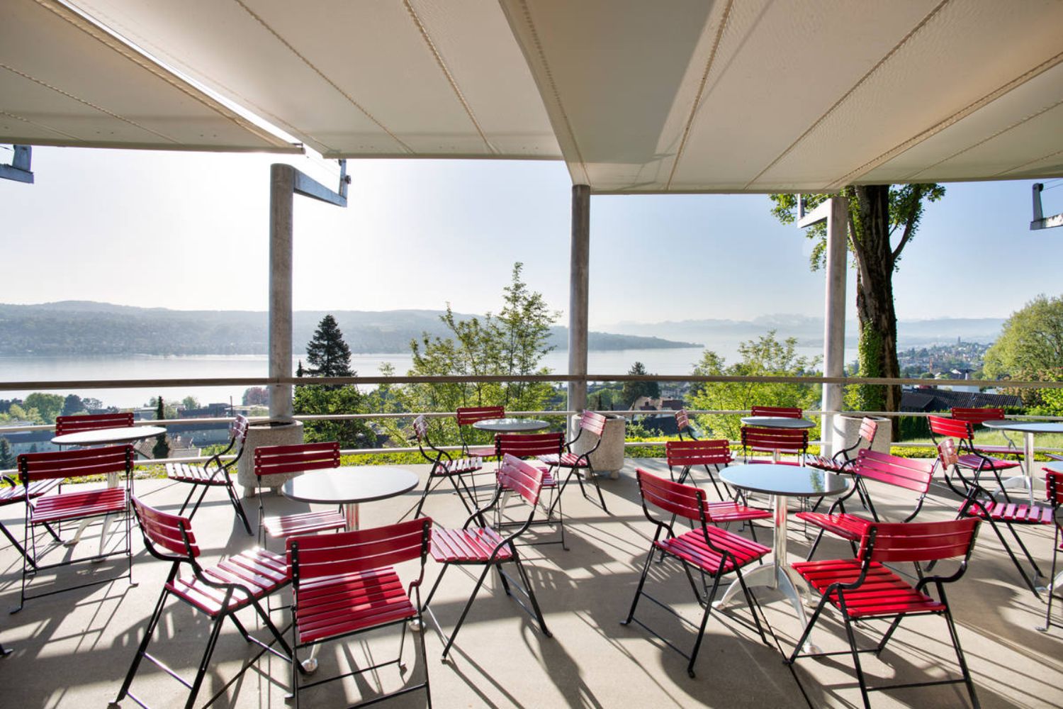 Tables and red chairs on a patio overlooking lake Zurich.