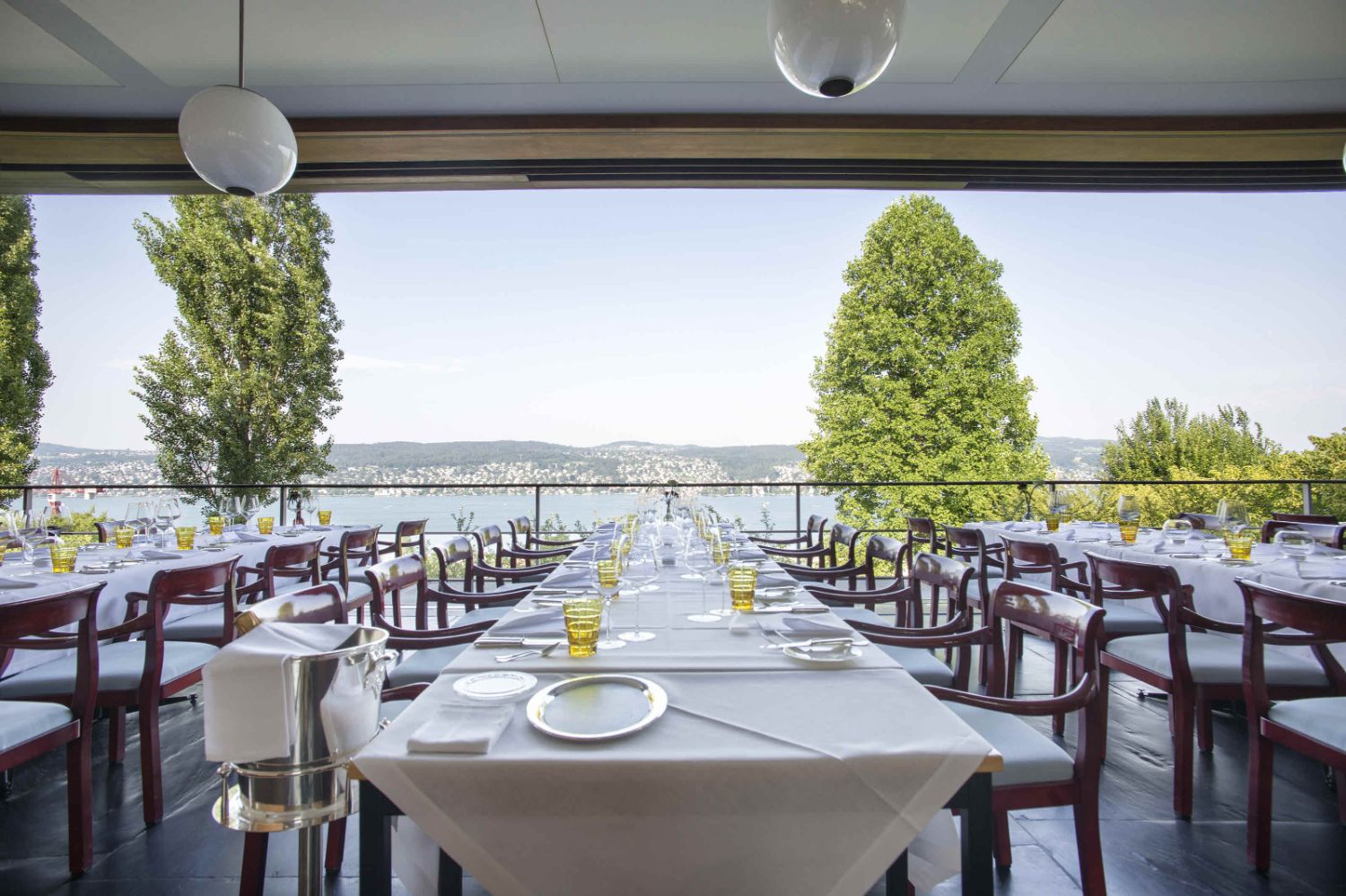 A long white table with tableware overlooking the lake of Zurich.
